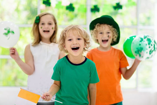 Three kids wearing Irish national colours celebrating St Patrick's Day with party balloons and decor